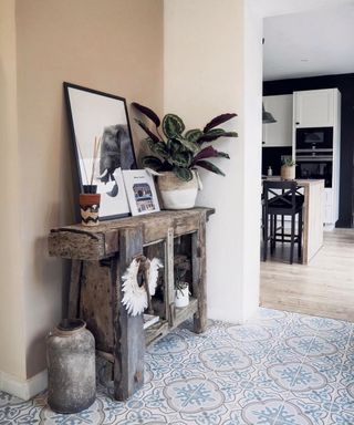 Blue and gray patterned floor tiles in entryway, with unique, rustic console table styled with African inspired artwork and objet.