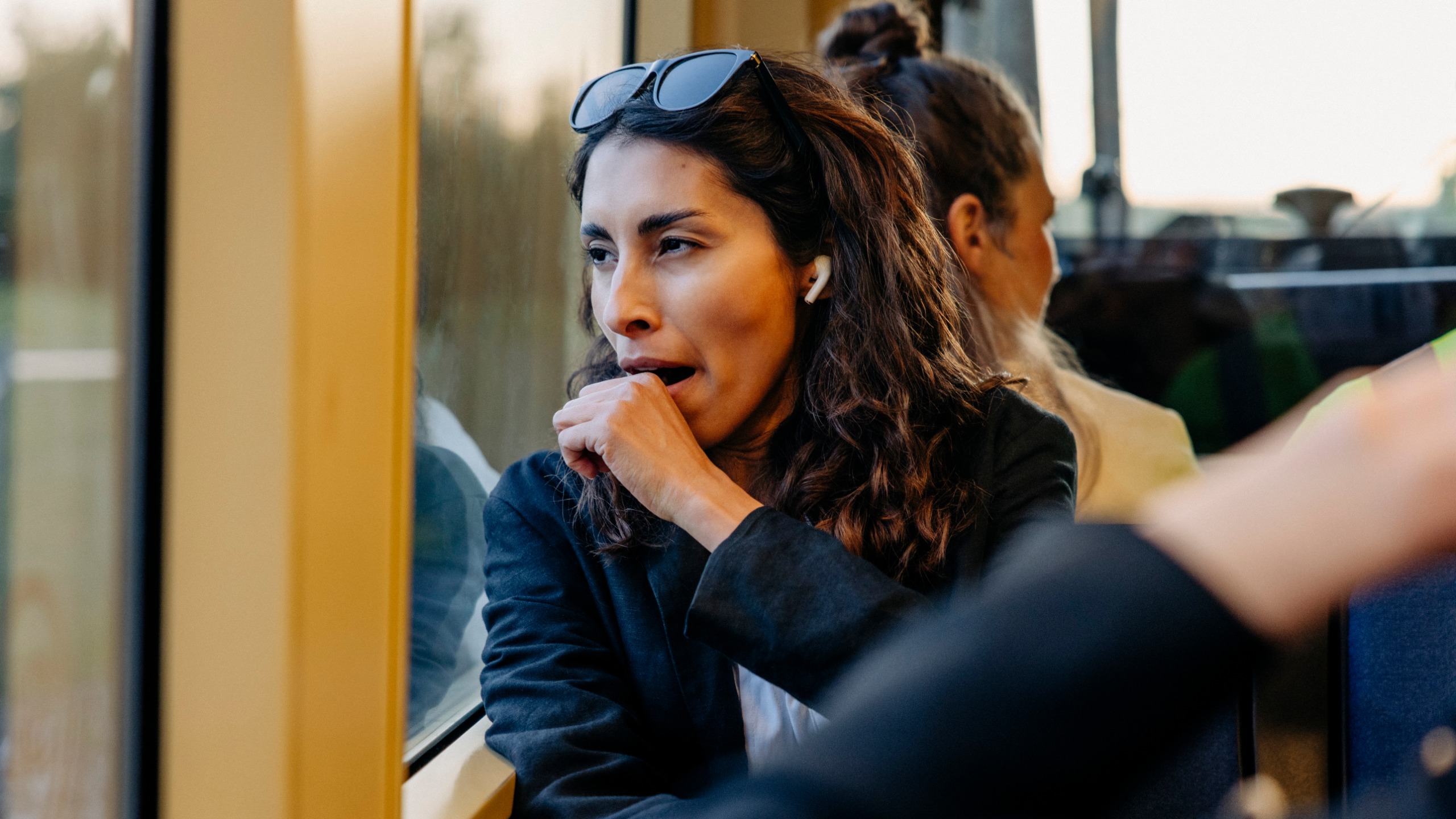 A woman on a train covers her mouth as she yawns. 