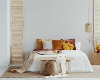 a boho bedroom with a white bed and velvet warm colored pillows on a white wall and a rattan hanging lamp