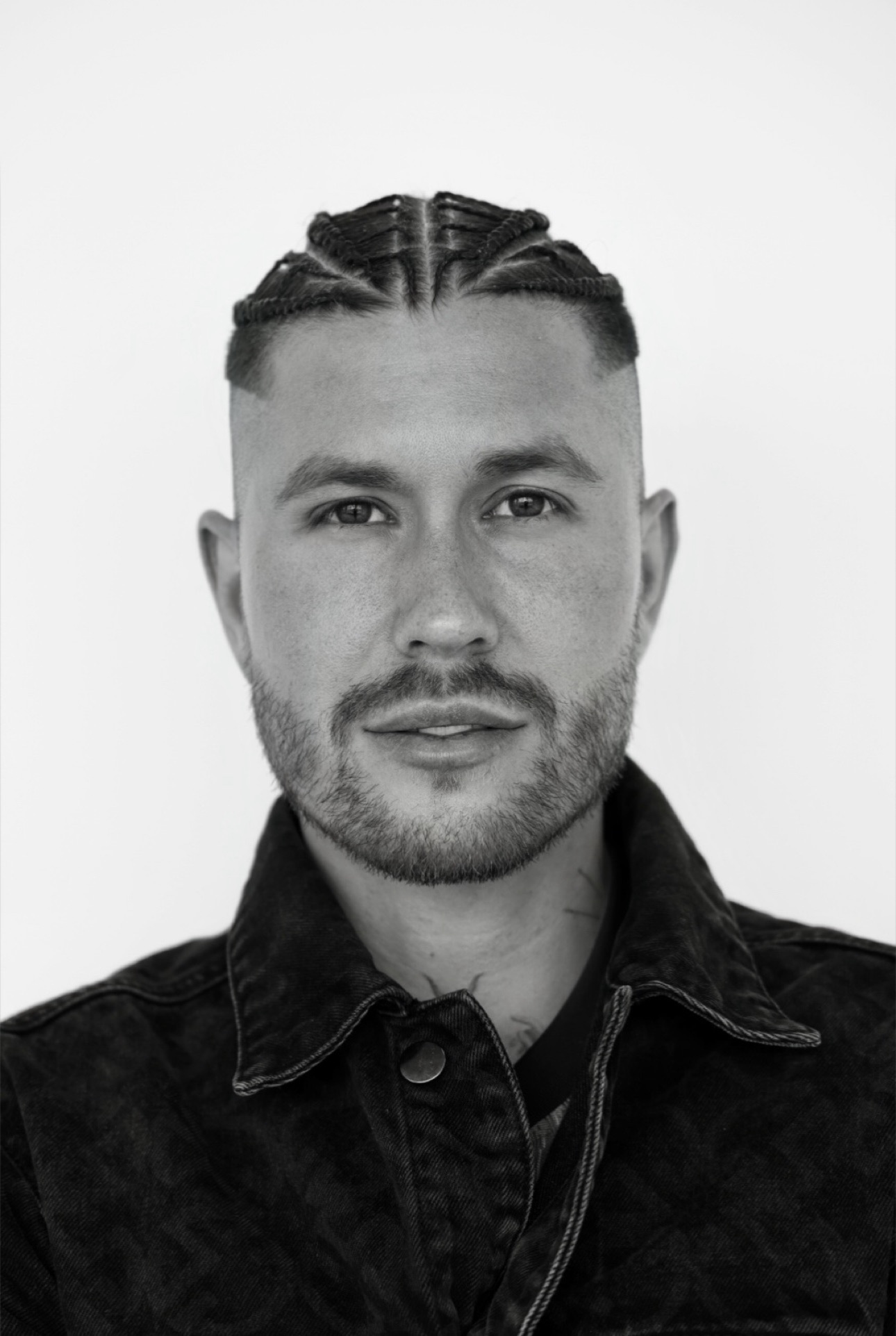 a black and white photo of a man in a black denim jacket with a beard