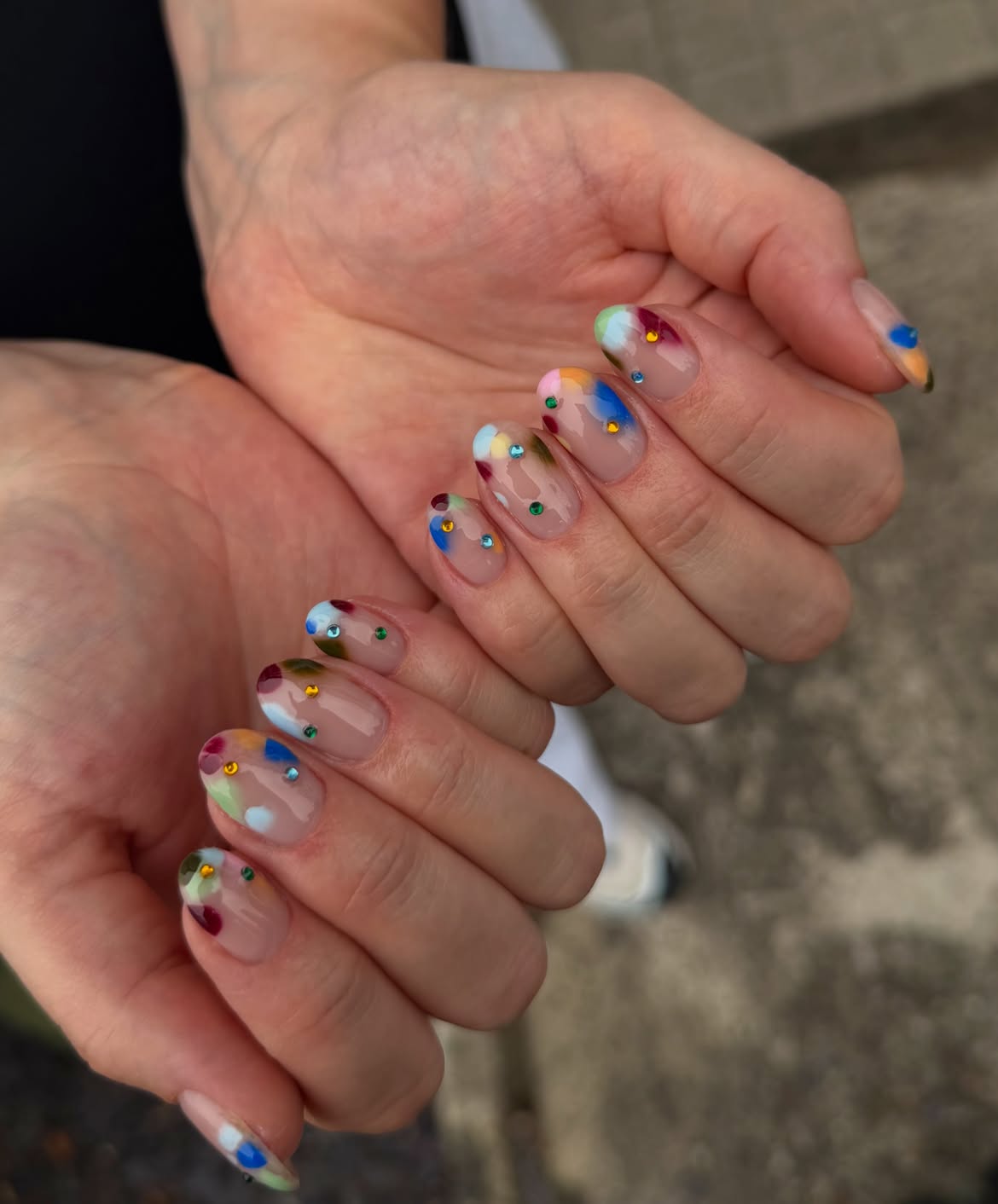 Bare almond nails with blurred rainbow color around the edges and multicolored gems
