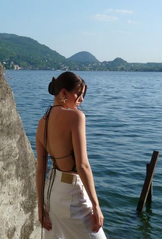 Shell jewelry trend shown on a woman wearing a black lace-up top and white jeans with starfish-shaped gold earrings.