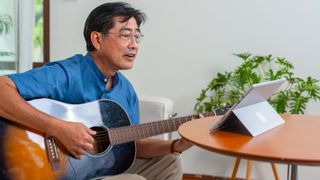 Man playing acoustic guitar while reading chords from a tablet
