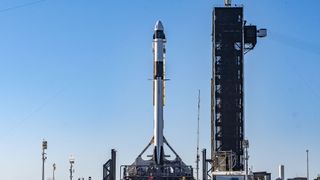 A white and black SpaceX Falcon 9 rocket stands on its launch pad ahead of launch.