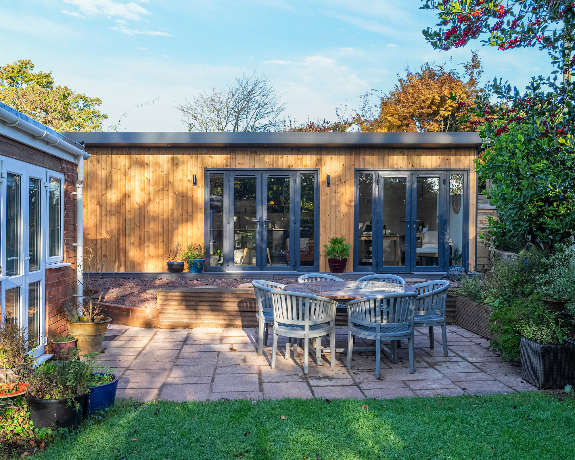 Garden annexe with wood exterior with patio and dining set in front and section of rear of house