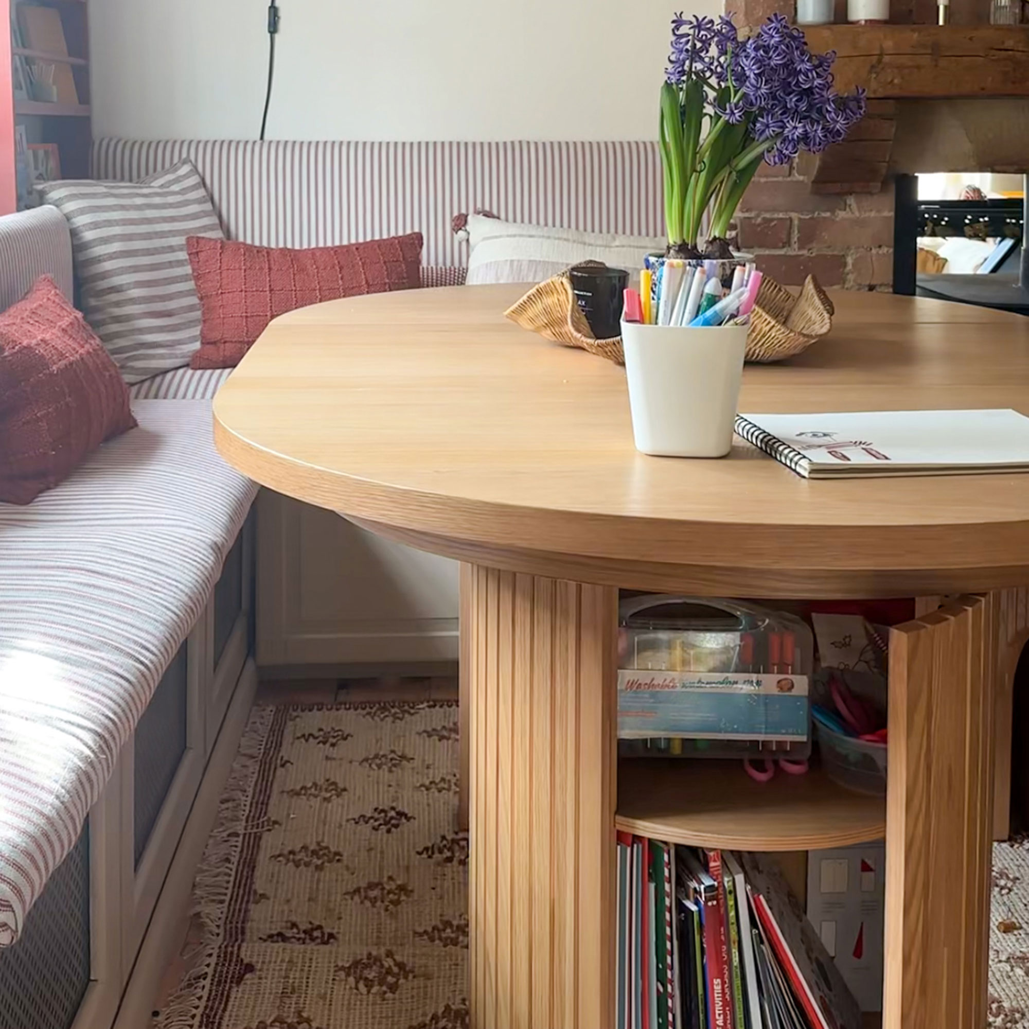 Banquette with striped upholstery around wooden kitchen table with hidden storage in centre