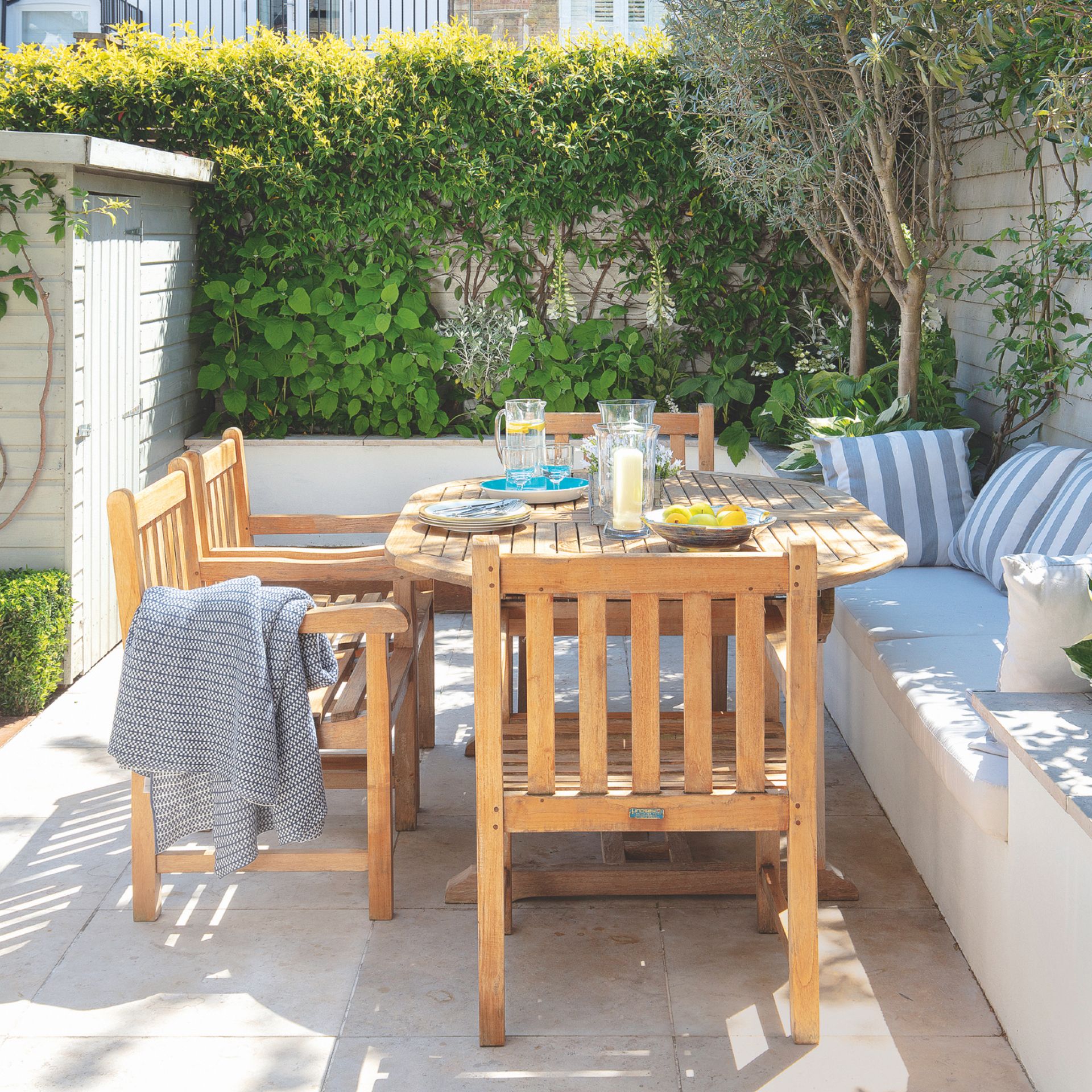 garden with paved area, bench seat to right, wooden table and chairs, growing plants, shed to left