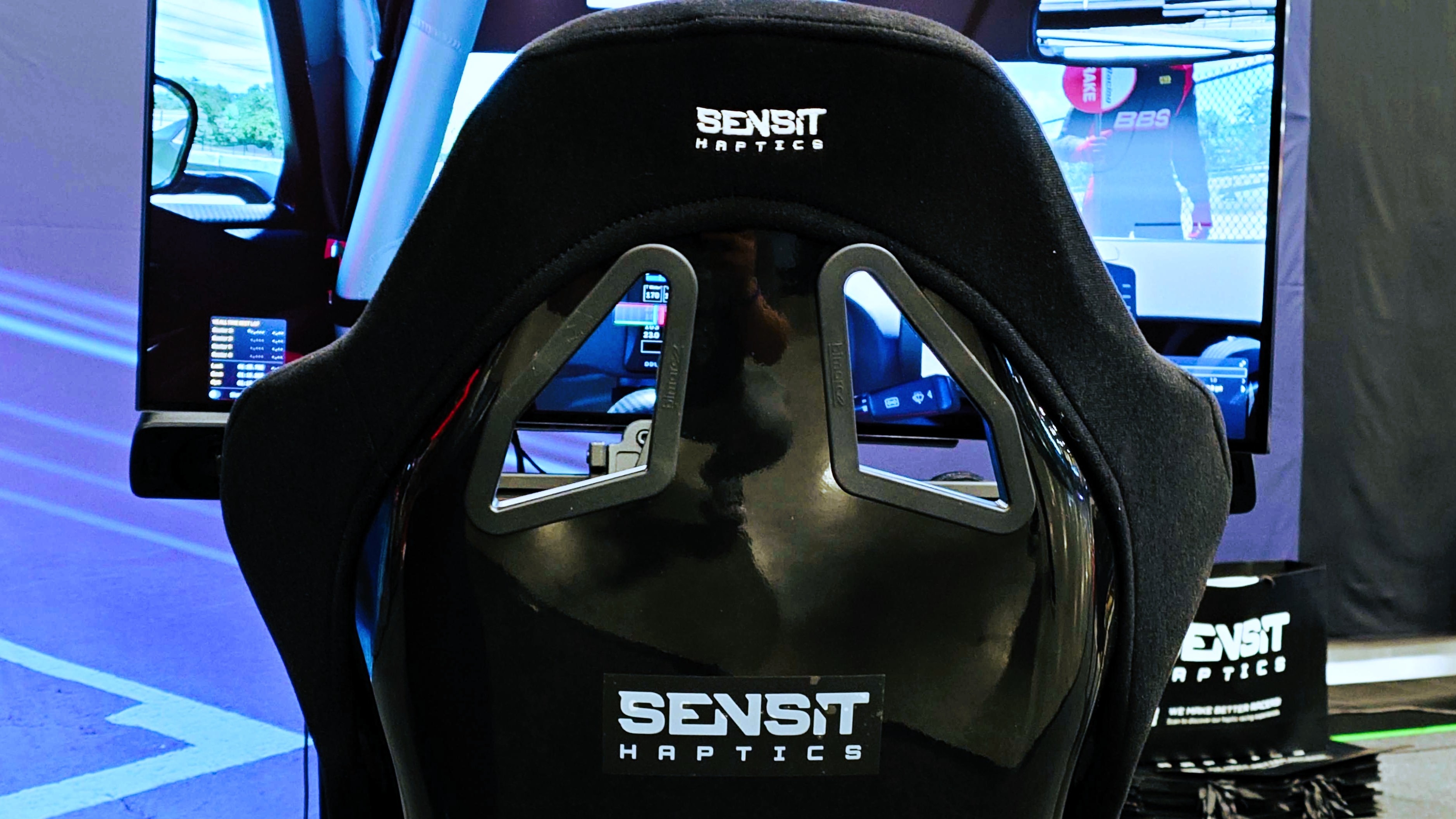 A photo of the rear of a Sensit Haptics racing seat in front of a screen showing iRacing. 