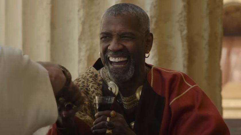 Denzel Washington laughs as he holds a glass of wine with one hand and shakes with the other in Gladiator II.