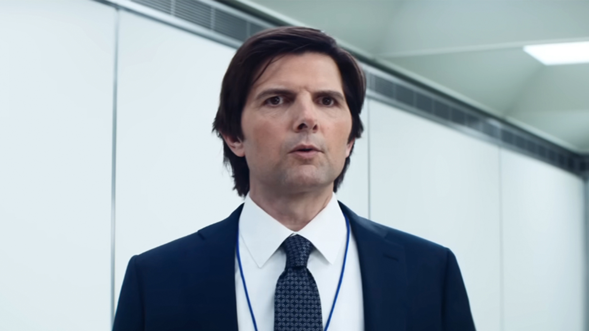 Adam Scott wearing a suit and tie in front of a white wall in Severance