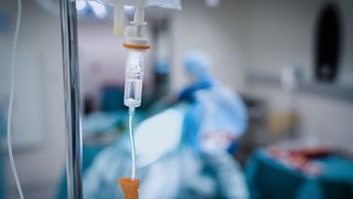 A close-up of an iV drip with a hospital environment blurred in the background