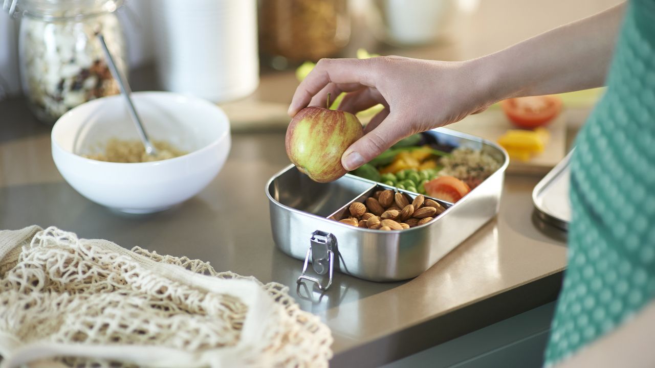 Woman packing vegan food into plastic free lunchbox at home