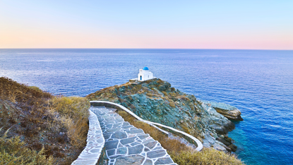 A paved path overlooking a blue domed church by the sea in Sifnos
