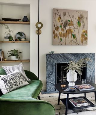 A living room with a blue marble fireplace, a rounded green velvet sofa and artwork on the walls