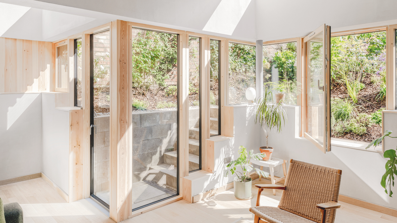 A bright, white room with pale window frames and large sunbeams looks out on a sunken garden.