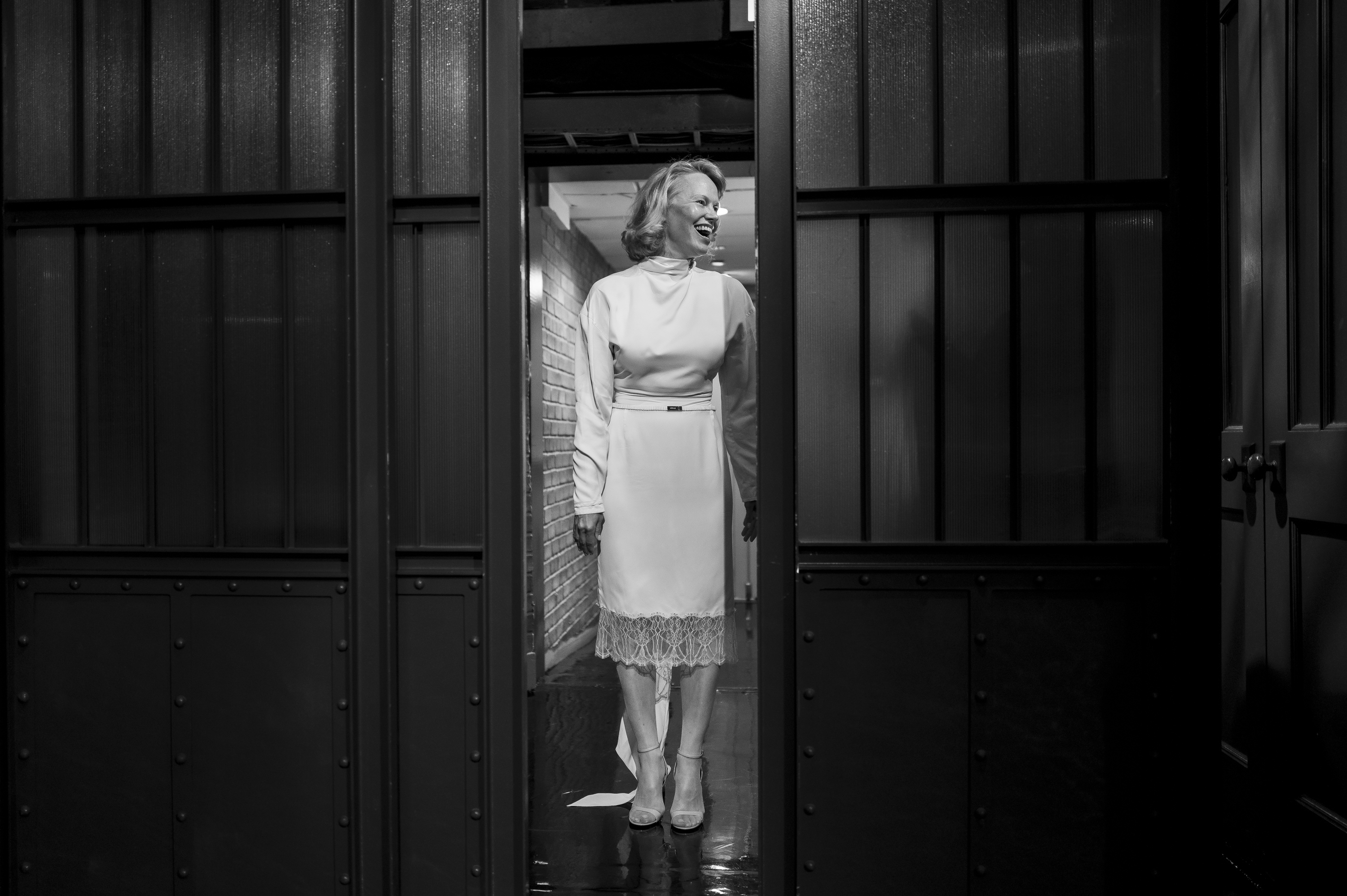 A black and white photo of Pamela Anderson in a white sleeved dress hemmed with lace.
