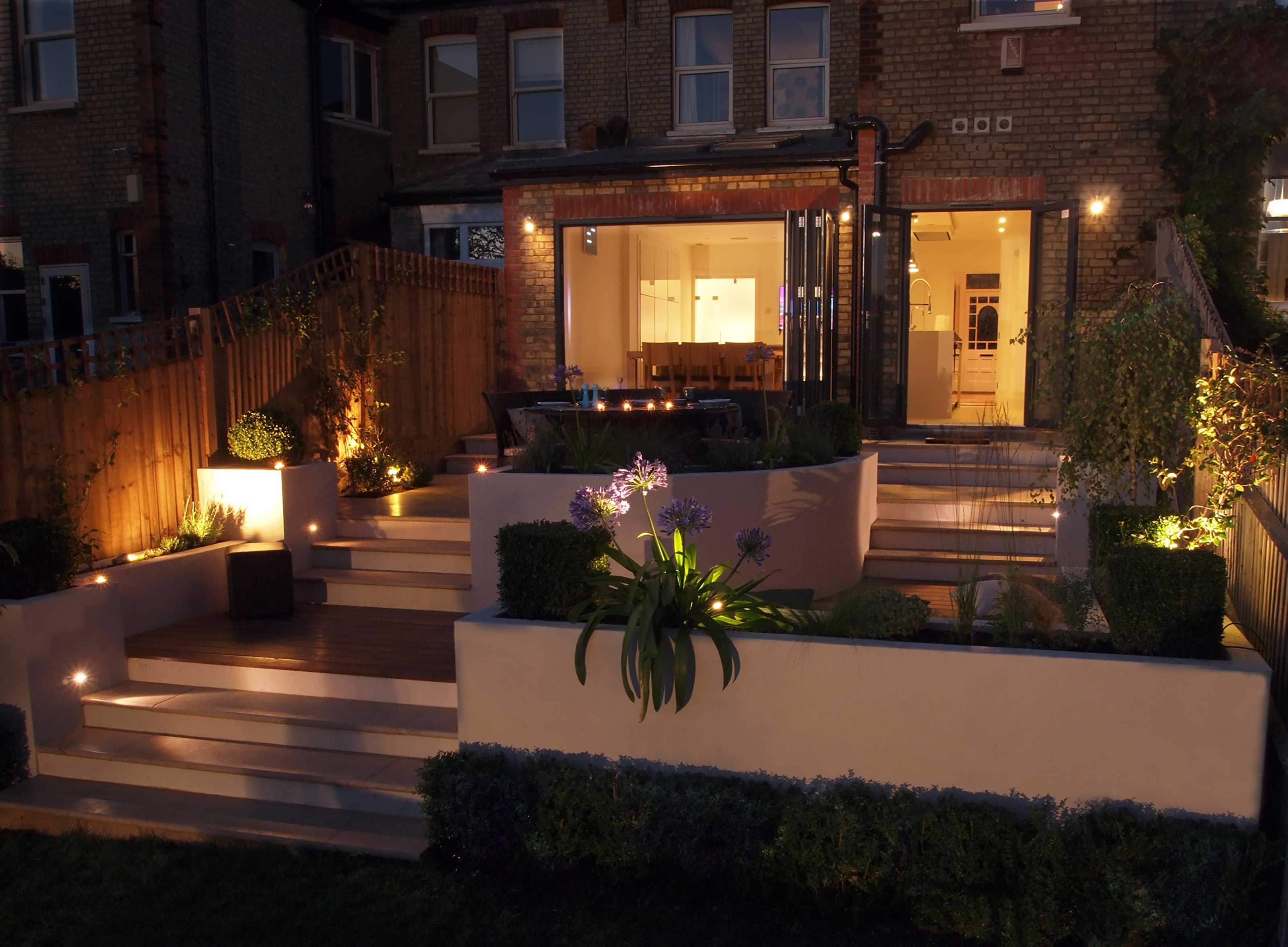 sloping garden ideas: tiered garden at night designed by Living Gardens