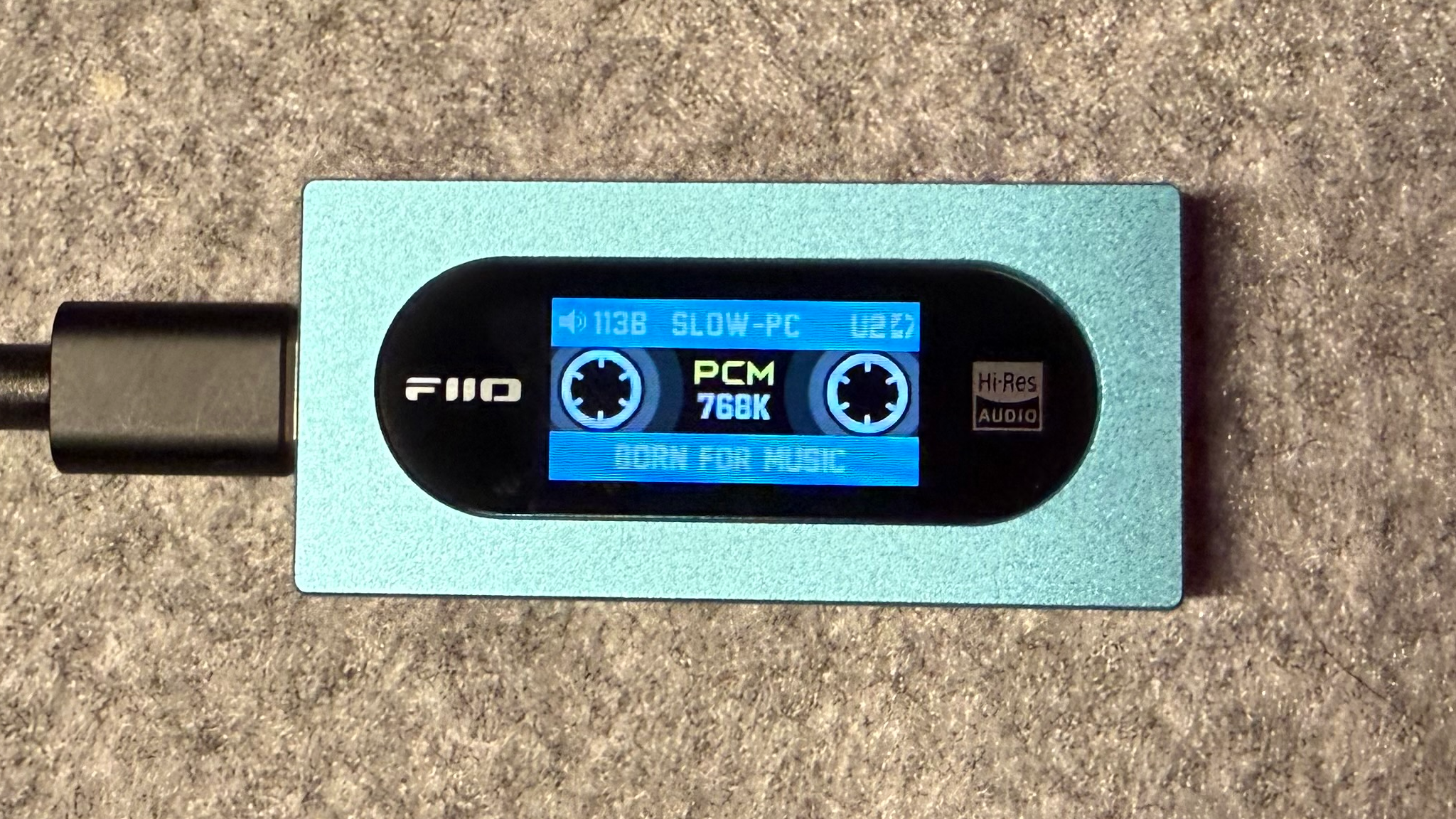 Фотография FiiO KA15, воспроизводящего музыку в формате PCM перед портативным ЦАП.
