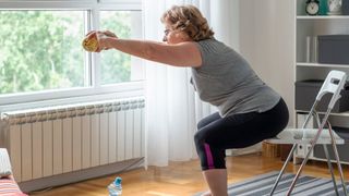 Woman reaching out in front with weights, squatting down on chair