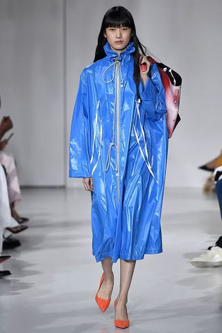 Model wearing a long blue raincoat walking down a catwalk