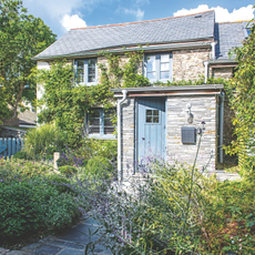 Front of the cottage with paved path, flower beds and blue front door. A renovated four bedroom Victorian house in Cornwall, home of Jill Stein.