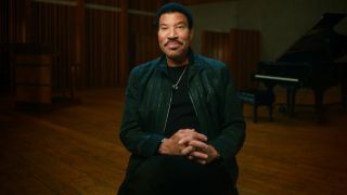 Lionel Richie in The Greatest Night in Pop sitting and looking at the camera.