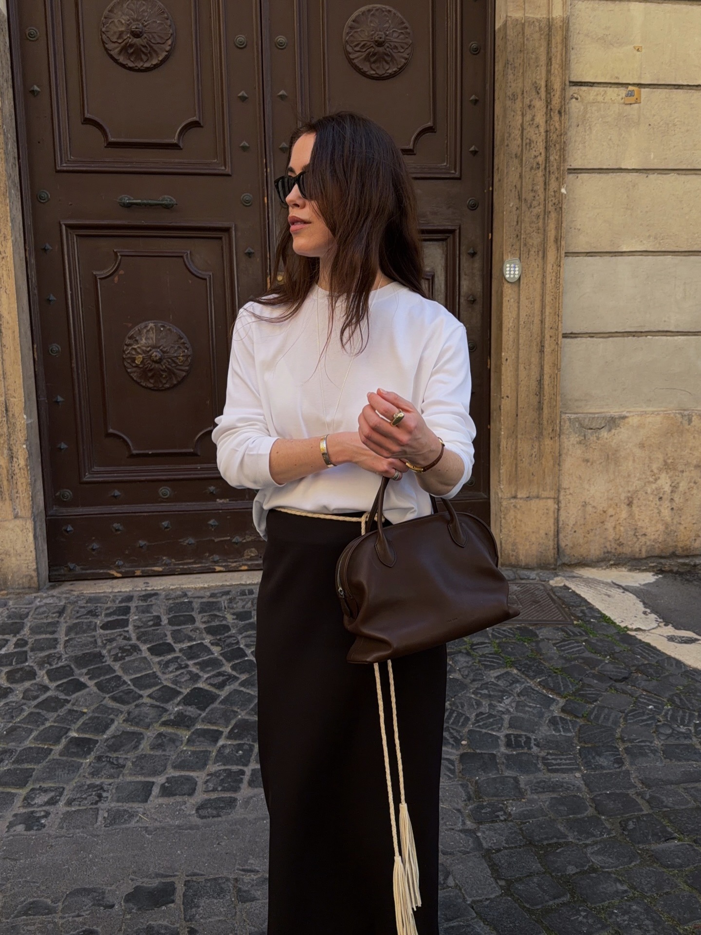 A woman wearing a white t-shirt with a brown handbag and long, brunette hair
