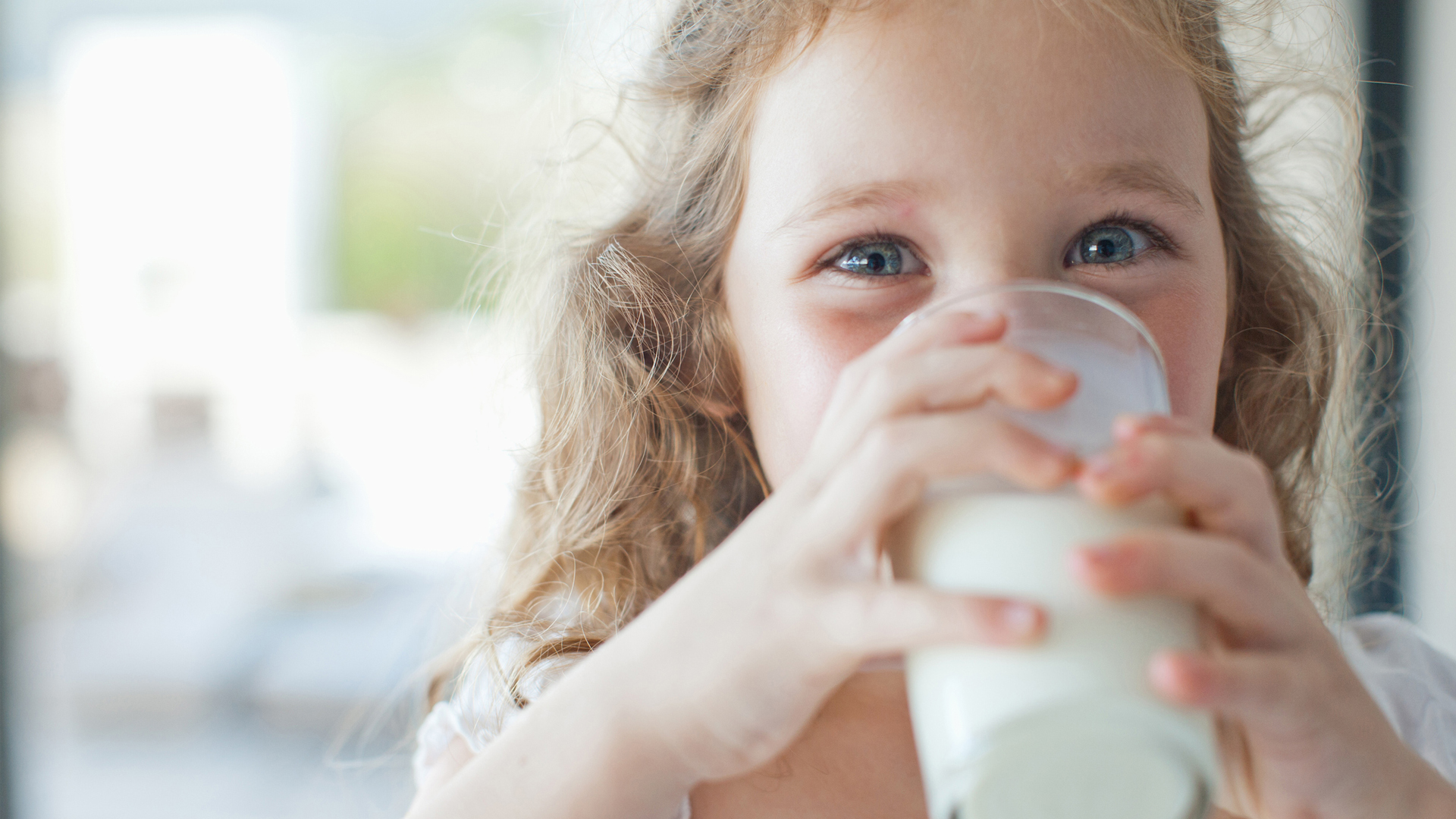 image shows a young girl drinking a glass of milk
