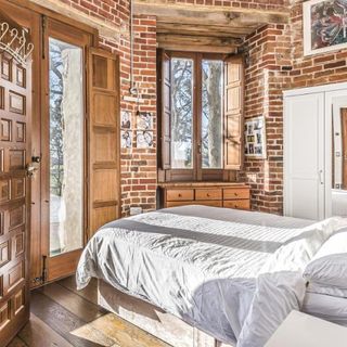 bedroom with brick wall wooden window and white bedlinen