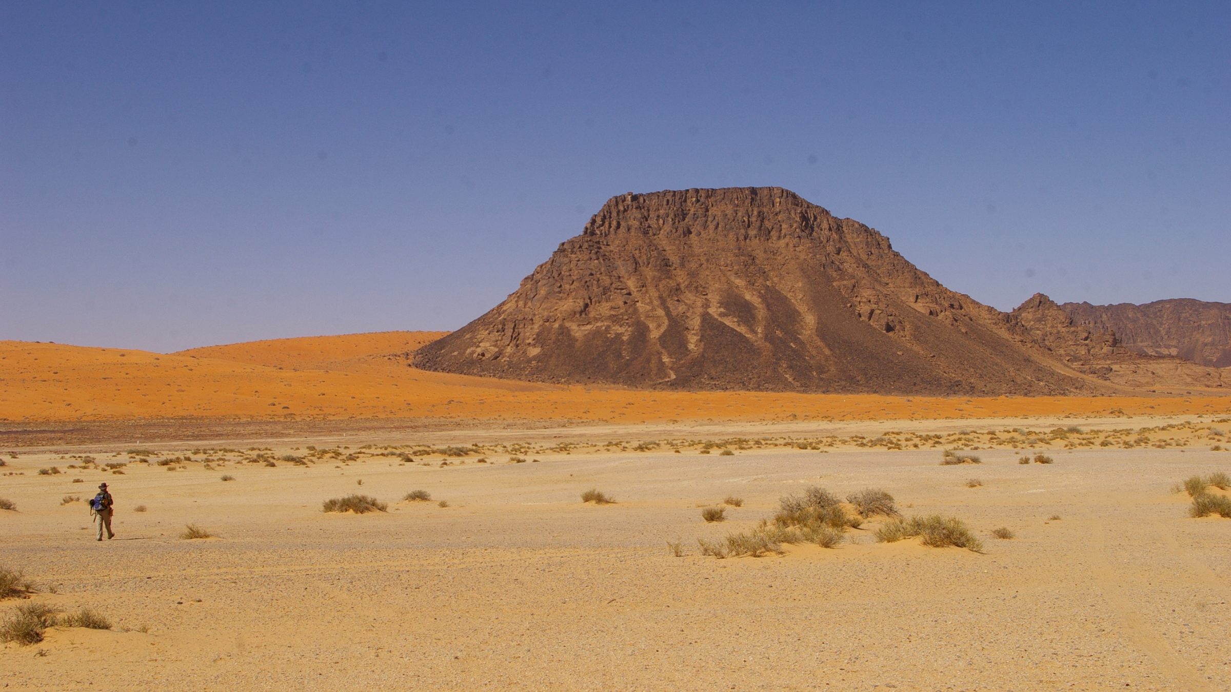 Mountain emerging from orange barren desert.