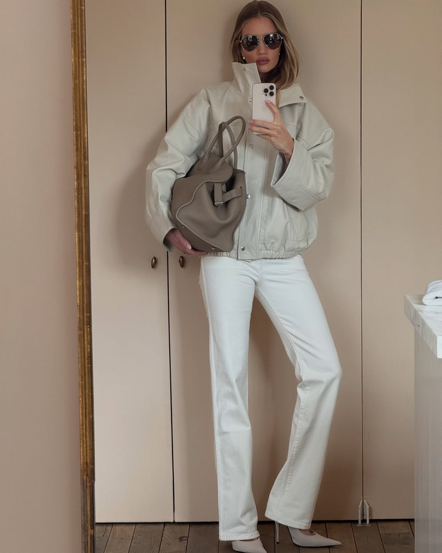 rosie wears white jeans, a funnel-neck jacket, and pointed toe heels.