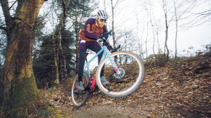 The Canyon Grizl CF SL 7 Throwback being ridden at speed with the front wheel off the ground in the woods, with lots of brown leaf matter on the ground