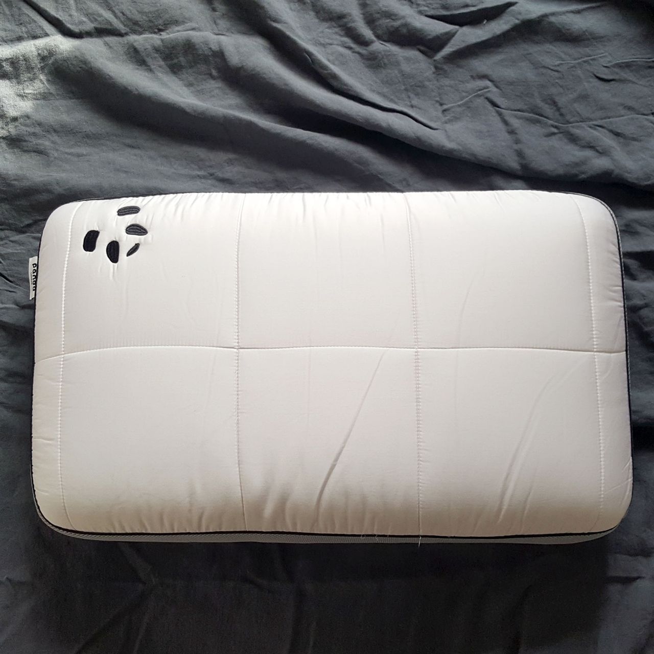 The Panda Hybrid Bamboo pillow on a bed with a white quilted top and panda logo.