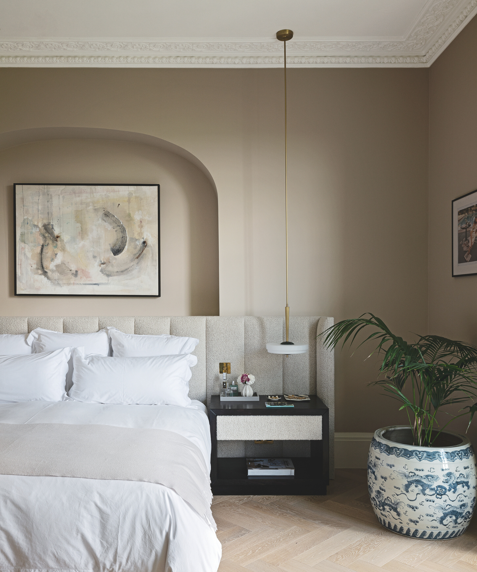 a neutral bedroom with a large bed with white bedding, light tan painted walls, a black nightstand, and a plant in a large ceramic pot