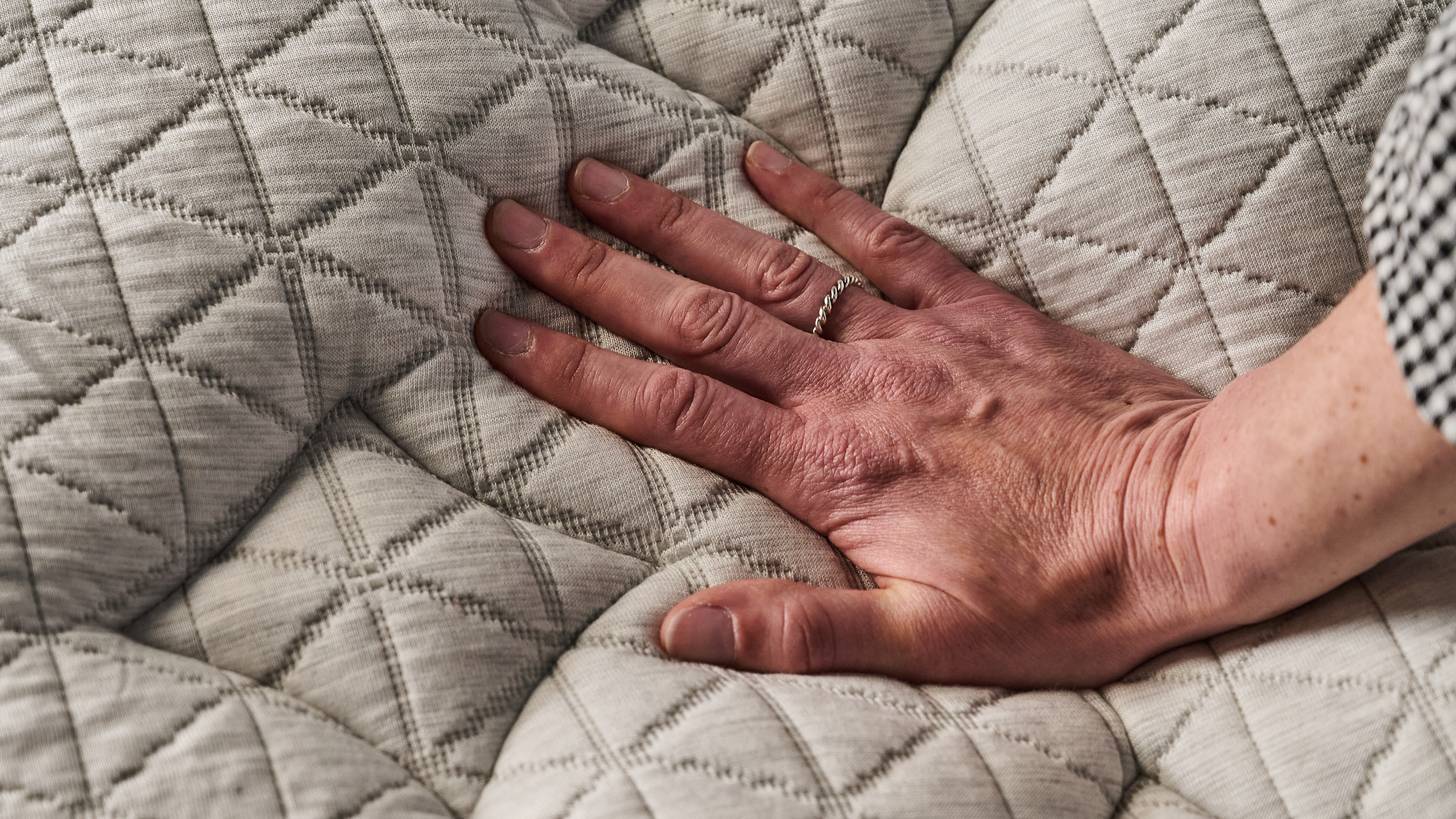 The image shows a mattress tester place her hand on the surface of the Helix Midnight Luxe to assess its temperature