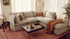an L shaped tan couch in a room with a red rug, a brown wood coffee table, and sheer drapes against the windows