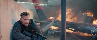 Chris Hemsworth as Tyler Rake, crouching away from a flaming plane, in Extraction 2