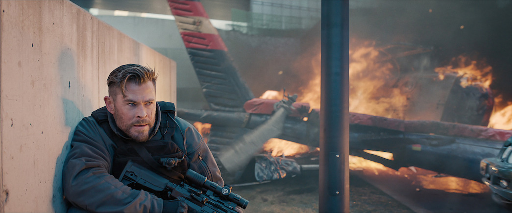 Chris Hemsworth als Tyler Rake, der sich in „Extraction 2“ vor einem brennenden Flugzeug duckt