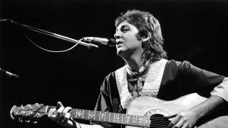 Paul McCartney playing acoustic guitar onstage
