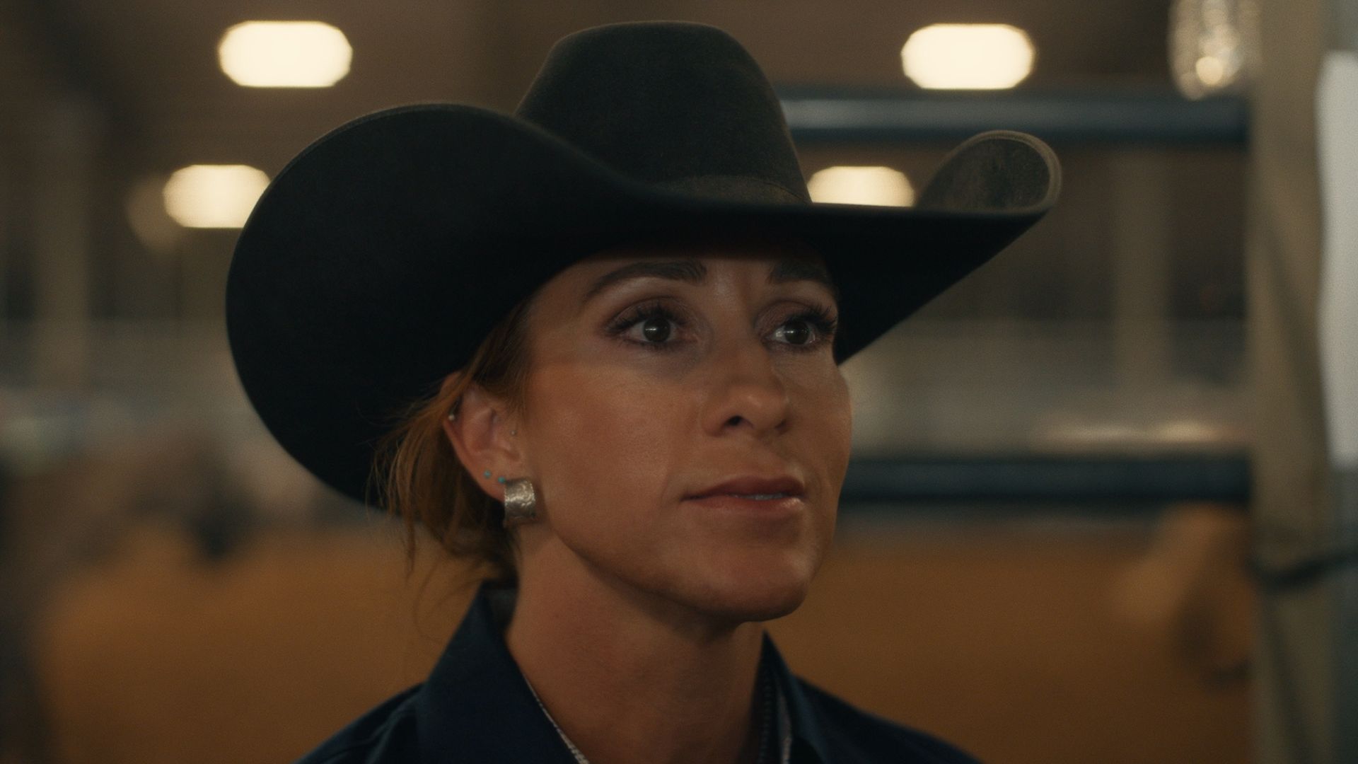 Angie Ayers wearing a cowboy hats looks on at something offscreen