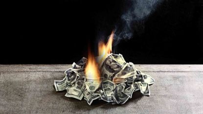 A pile of hundred-dollar bills is on fire on top of a table