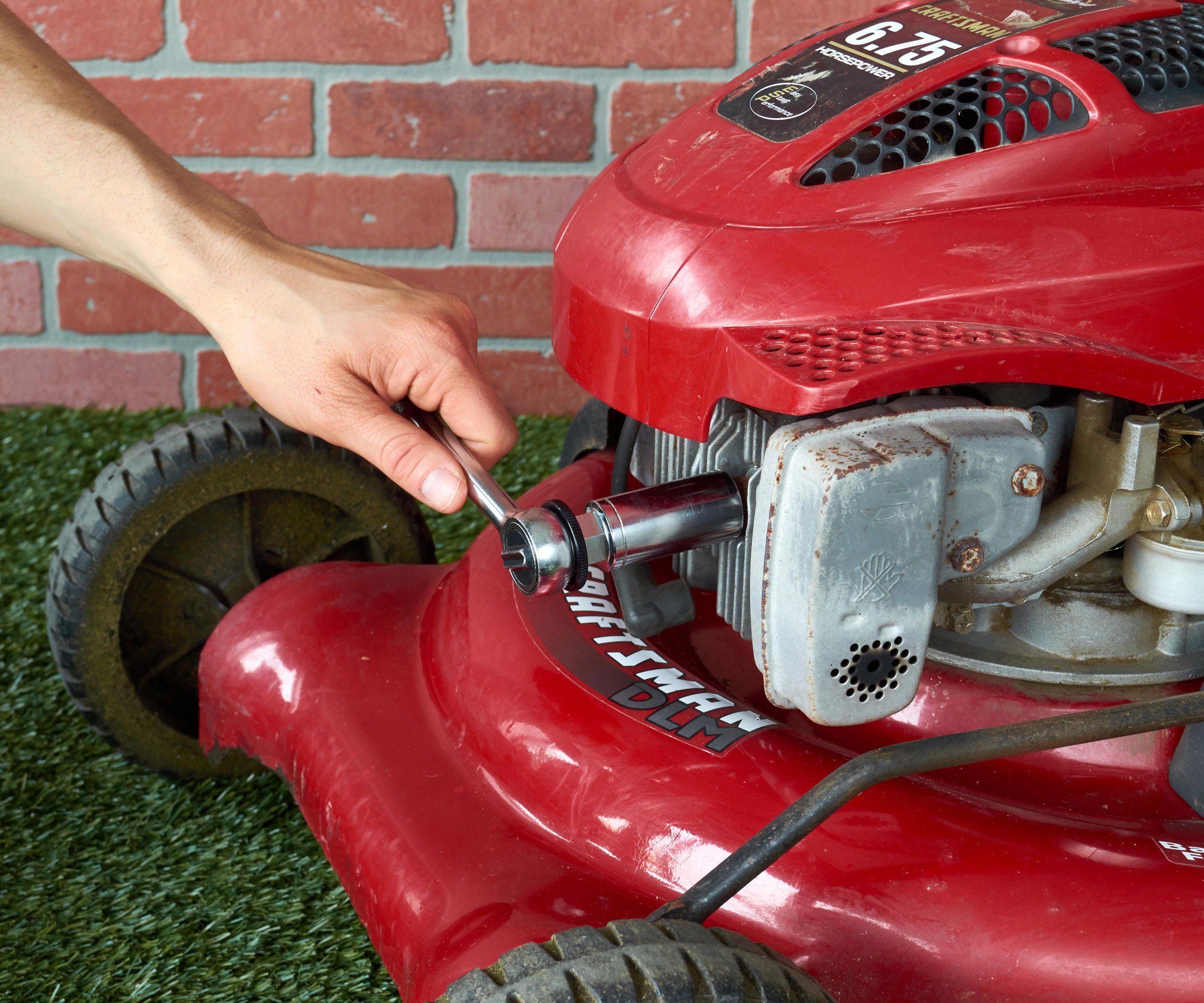 hand making adjustments to red lawn mower during standard maintenance checks