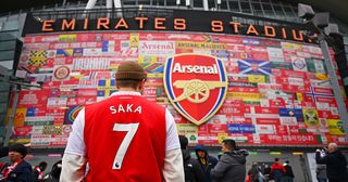 Arsenal fan wearing an Bukayo Saka of Arsenal shirt stands outside the We All Follow The Arsenal stadium wrap around prior to the Premier League match between Arsenal FC and Brentford FC at Emirates Stadium on February 11, 2023 in London, England.