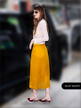 Dakota Johnson wearing a sheer white top, yellow slip skirt, and burgundy Gucci kitten heels.