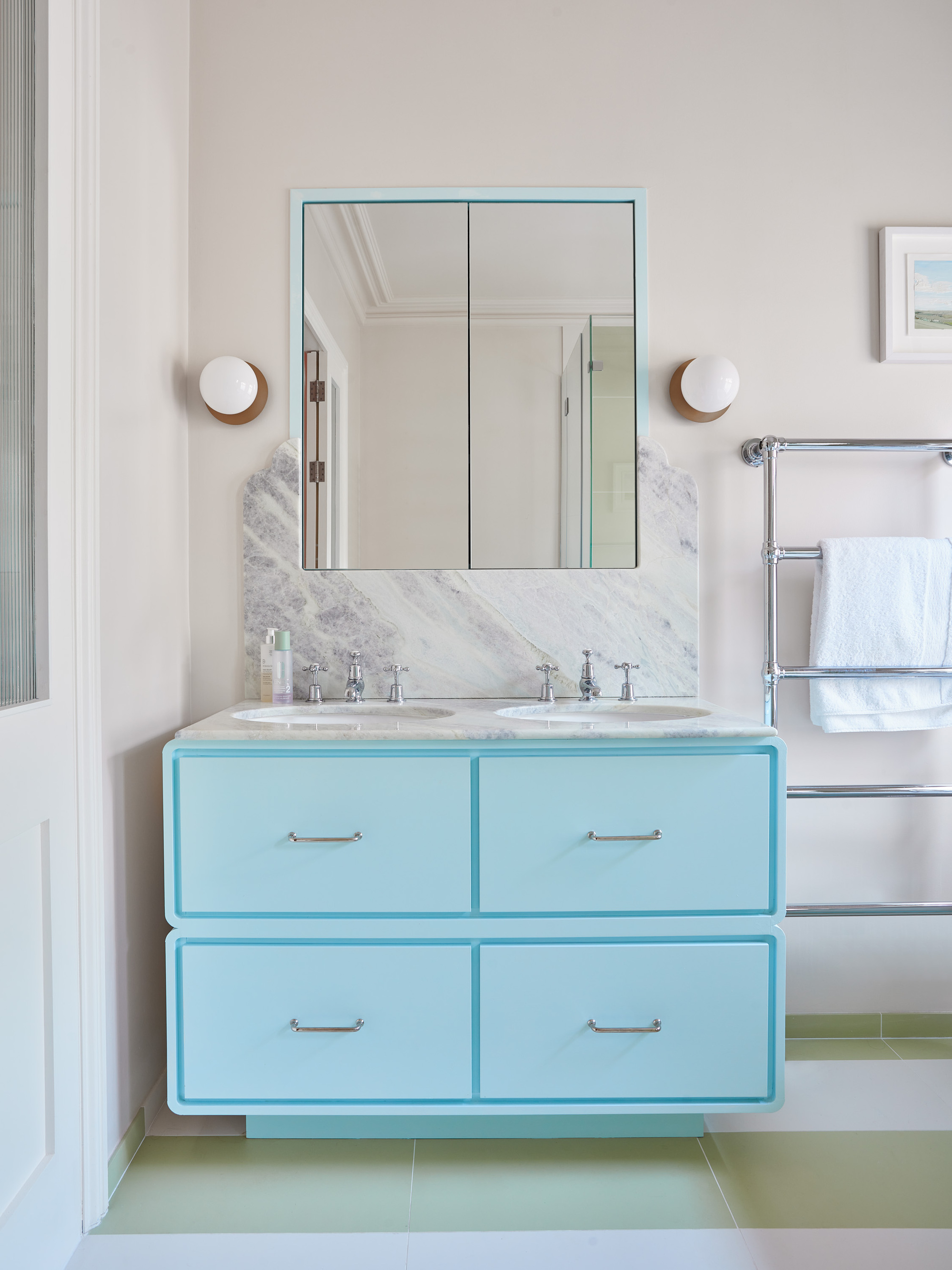 modern bathroom with bright light blue vanity with drawers, mirrored cabinet, marble vanity and backsplash, heated towel rail and green and white floor tiles