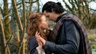A young couple gaze into each others' eyes and hold hands in a forest