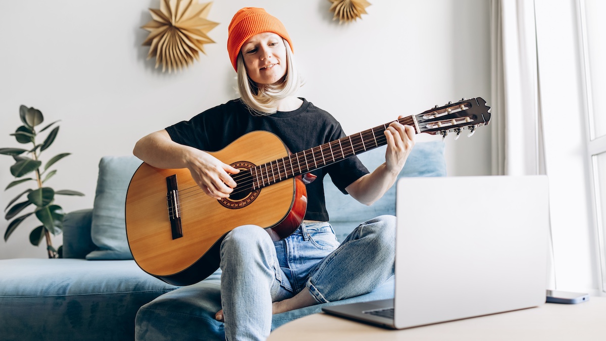 Woman in orange hat plays classical guitar in front of a laptop
