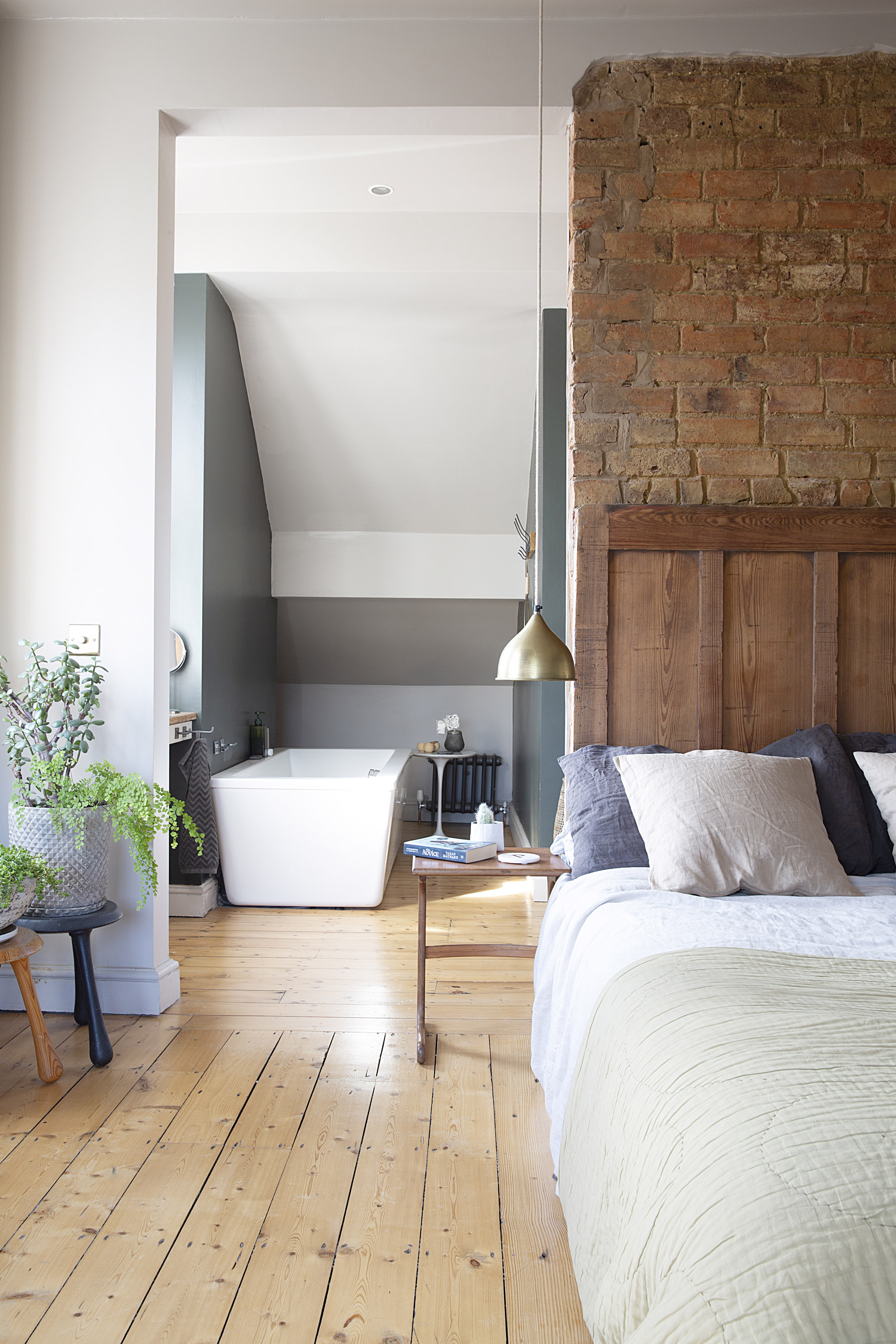 modern loft bedroom with open en-suite, free-standing bath, plants and exposed wood flooring