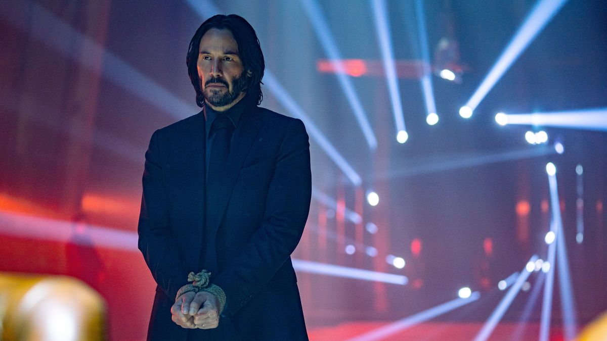 Keanu Reeves as John Wick, with spotlights behind him, in John Wick: Chapter 4