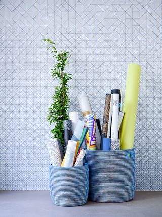 Two blue baskets containing rolls of patterned paper and a plant sit on the floor in front of a pale blue wall with geometric designs